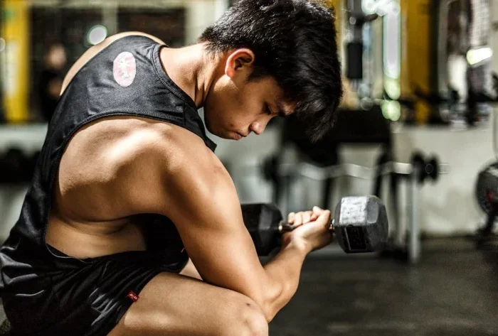 A man performing a bicep curl with a dumbbell in a gym, focusing on muscle growth and strength training.