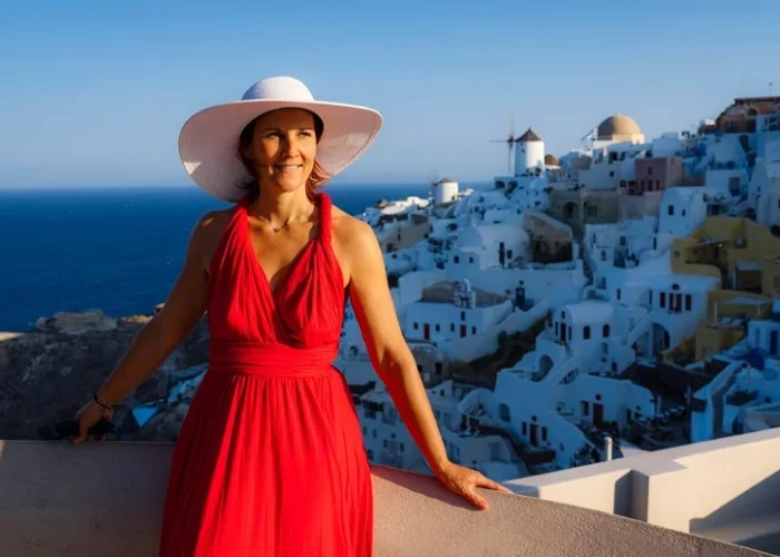 Woman in a red dress admiring a stunning Moroccan village with white buildings by the sea.