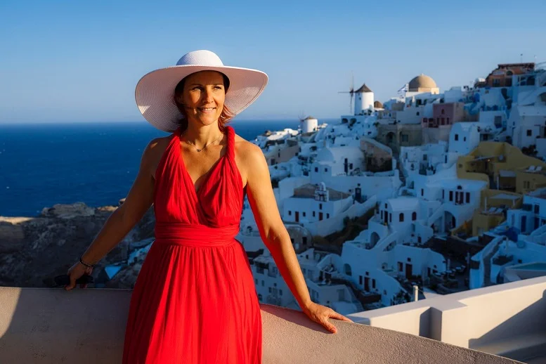 Woman in a red dress admiring a stunning Moroccan village with white buildings by the sea.