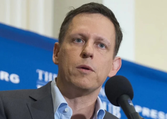 Matt Danzeisen speaking at a professional event with a microphone in front of him and a blue backdrop featuring an organization logo.